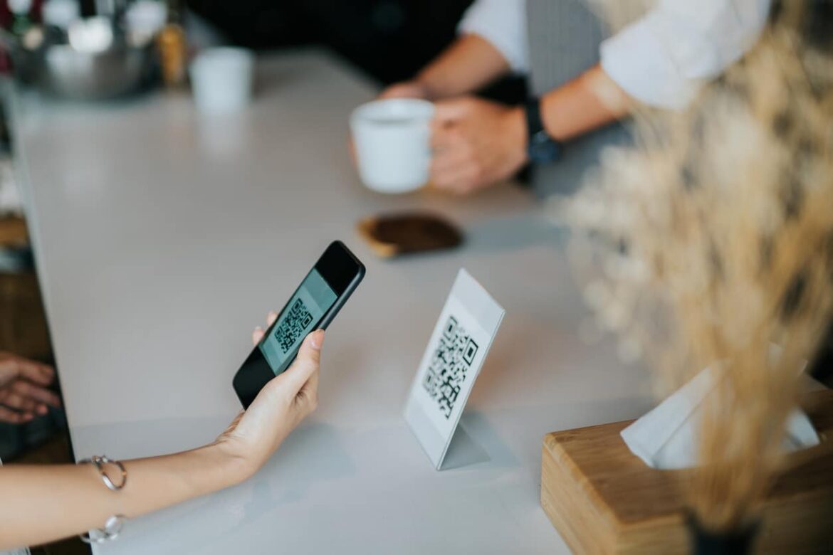 Woman’s hand holding smartphone, scanning barcode for contactless payment in the cafe